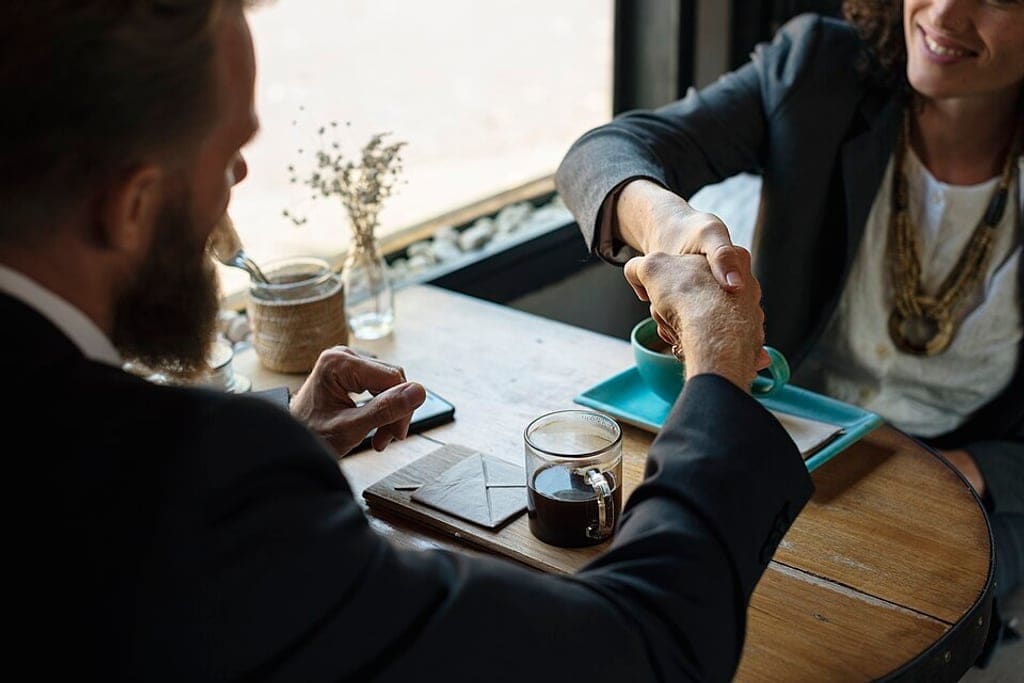 Two people shaking hands over coffee.