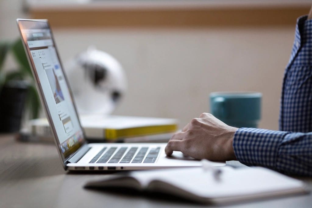 A person working on a laptop beside a notebook.